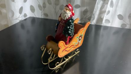A vintage 3.5" Santa Claus Christmas ornament featuring a hooded cloak and backpack Keepsake Christmas tree ornament featuring a wooden sleigh