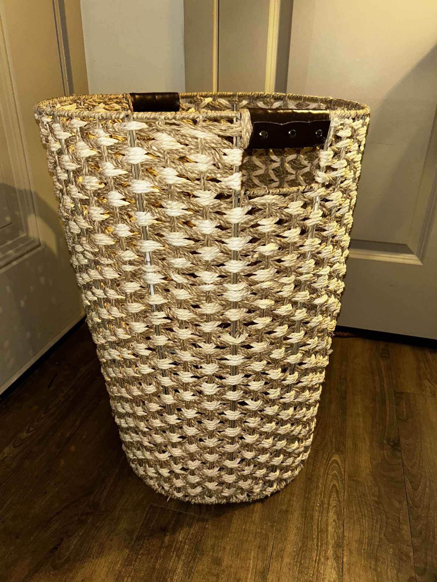 a handwoven wicker laundry hamper with leather handles.