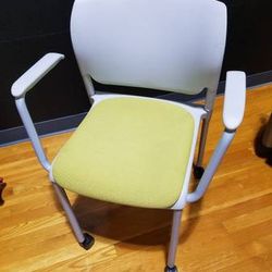 Green chair on casters. Flex back. 1 leg is bent.

