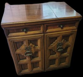 vintage 1970s rolling wooden sewing machine cabinet, featuring a fold-out top surface, two faux-top drawers, and cabinet doors with ornate geometric p