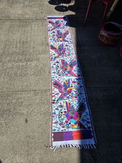 Beautiful white fabric table runner decorated with handcrafted embroidery featuring vibrant hummingbirds and multicolored flowers.
