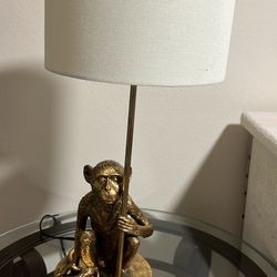 antiqued gold or golden polyresin monkey table lamp with a white shade. 