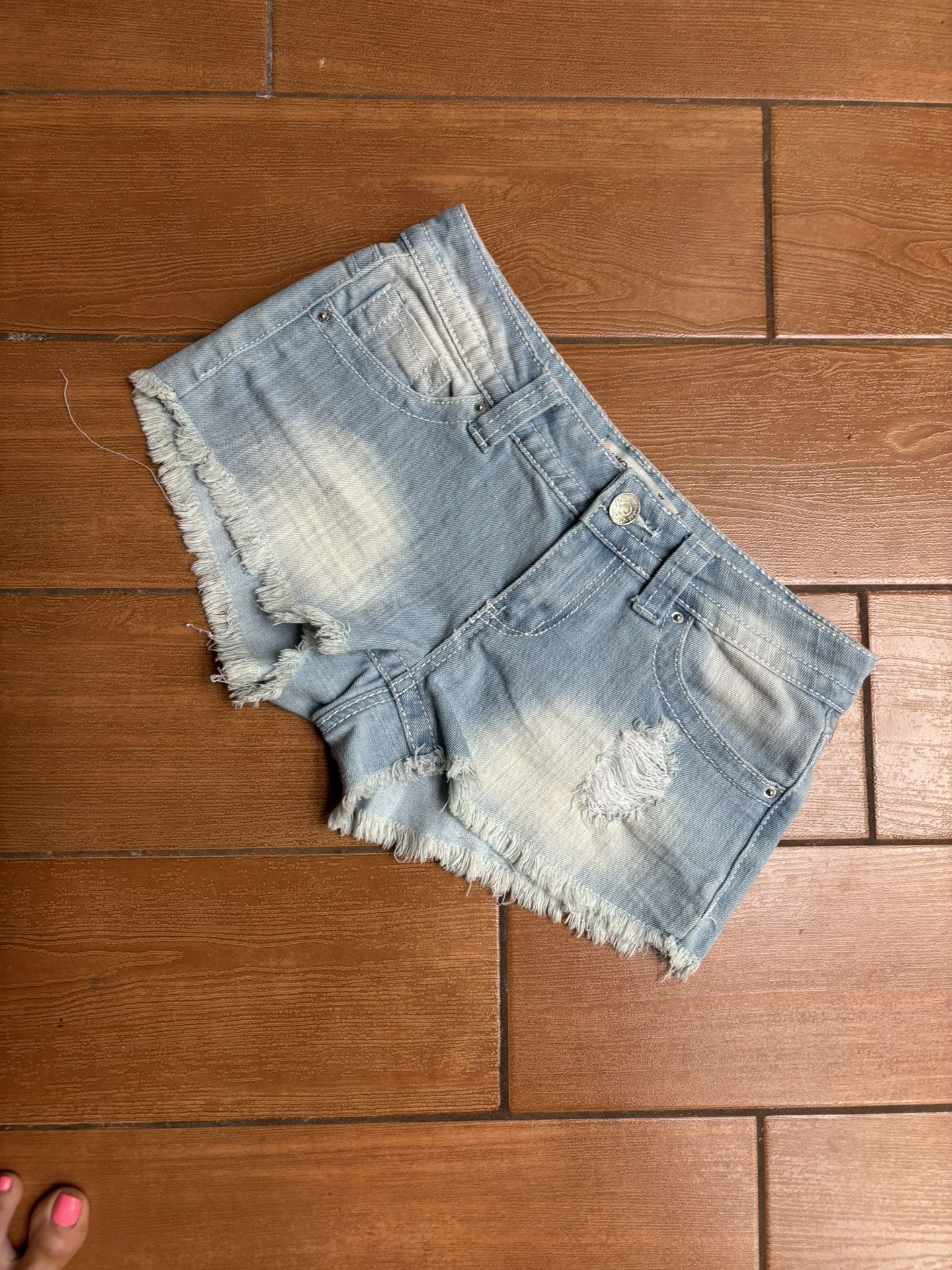 These blue jean shorts by Almost Famous feature a distressed design with frayed hems and a faded wash, offering a trendy and casual look. The raw edge