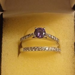 This jewelry is a sterling silver bridal set featuring a round-cut amethyst as the center stone, flanked by smaller accent stones, likely white sapphi