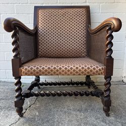 Antique oak Bergere armchair featuring barley twist legs, arms, and stretchers, with cane paneling sides and caster wheels