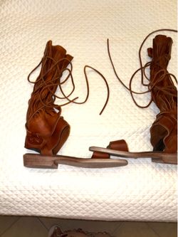 Free People boho-style gladiator sandals feature brown leather fringe and wrap-around laces. The ankle boot design has multiple fringes and laces that