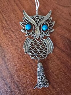 Eye-catching owl pendant necklace in old silver tone with bright blue accent eyes. Intricate filigree body and layered wing detail create elegant text