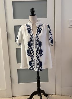 This white blouse with navy blue floral print is a popular style available at various women's fashion stores. It features a mandarin collar with ruffl