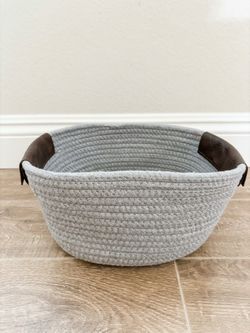 grey woven cotton rope storage basket with dark brown faux leather handles.