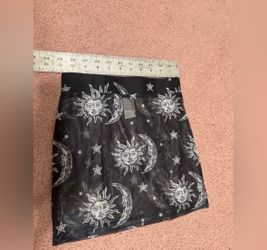 Sheer black mesh mini skirt featuring white sun, moon, and star motifs. Elastic waistband for easy wear. Layer over shorts or tights for a celestial l