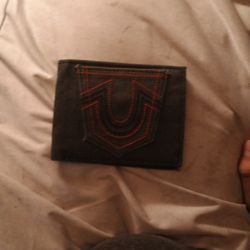 a True Religion Men's black leather bifold wallet with red stitching and a horseshoe logo. 
