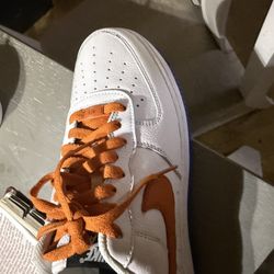 This is a white Nike Air Force 1 low-top sneaker with an orange swoosh and laces, and a blue outsole. 