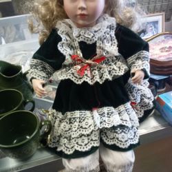 vintage collectible porcelain doll, featuring a green velvet dress adorned with white lace and a decorative ribbon. 