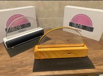 Modern digital alarm clock with a transparent semi-circular LED display. The base is available in a white plastic finish or a light wood grain finish.