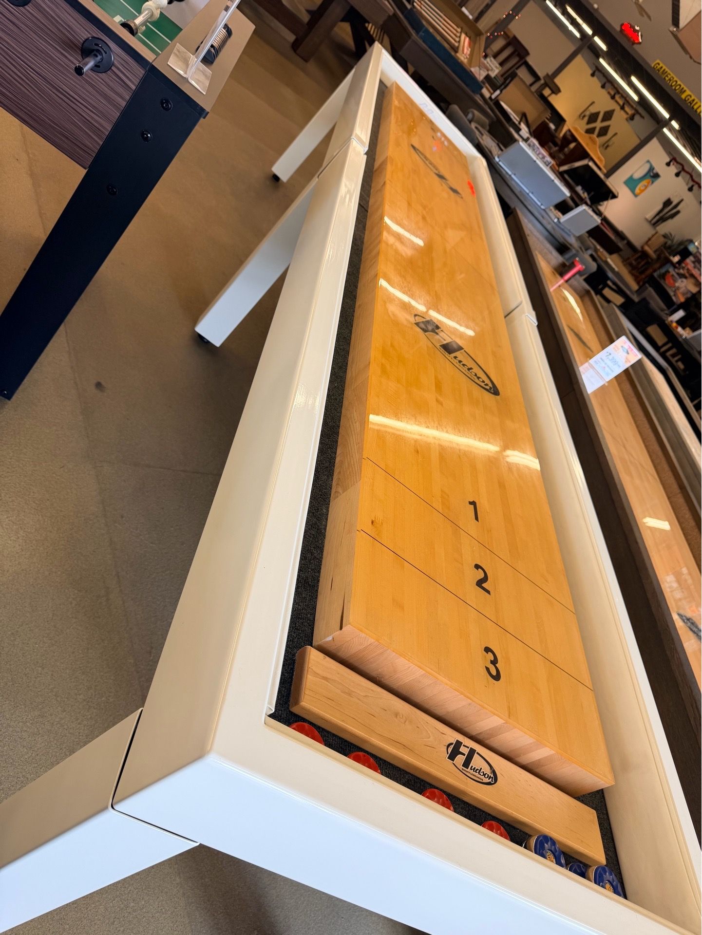 12' Hudson Metro Shuffleboard Table featuring a sleek white cabinet and a light-colored maple playfield.