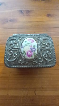 Gorgeous vintage jewelry trinket box made of cast metal with ornate raised floral designs on all sides.
The lid features an oval porcelain insert with
