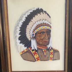The image shows a framed piece of vintage crewel embroidery depicting a Native American chief wearing a full feather headdress.