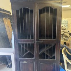 dark wood wine storage cabinet featuring upper shelving and lower X-shaped racks behind iron barred doors
