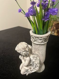 Detailed stone-look resin figurine features a kneeling cherub in prayer positioned next to a small cylindrical vase. The piece has a weathered gray fi