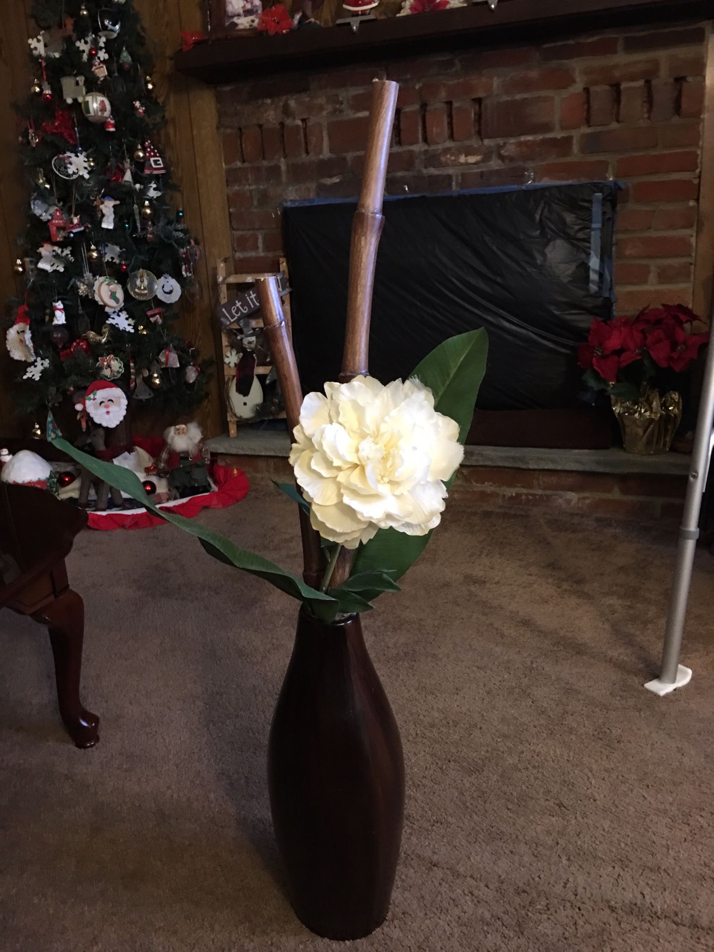 Tall wood vase with white flower and greens and bamboo.