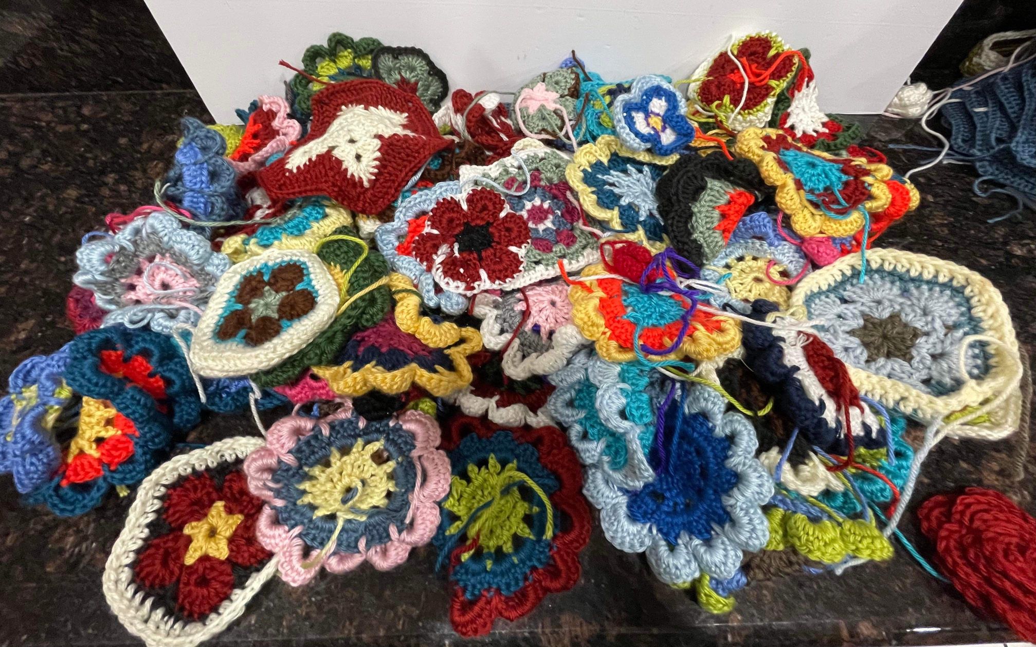 Large assortment of crochet granny squares. They are made of colorful acrylic yarn. There are approximately 100 small pieces, 50 blue/white, a finishe