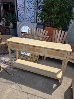 Bohemian-style light wood console table featuring three front drawers with rattan detailing and an open bottom shelf.