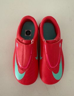 Nike Kids' Mercurial Vapor 16 Club soccer cleats in a vibrant "Ember Glow/Aurora Green" colorway.
