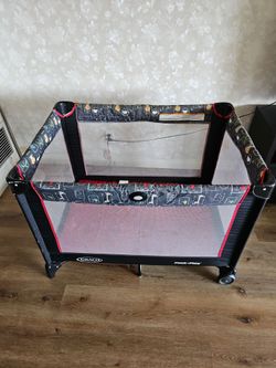 black and red Graco Pack 'n Play portable playard featuring mesh sides and a button fold mechanism on the rail.