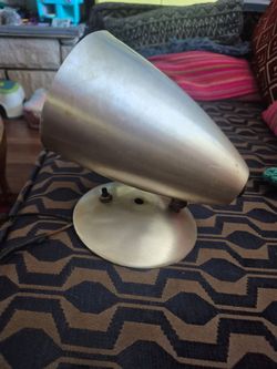 This vintage wall sconce features a cone-shaped spun aluminum shade and a metallic base, often associated with mid-century modern atomic lighting desi
