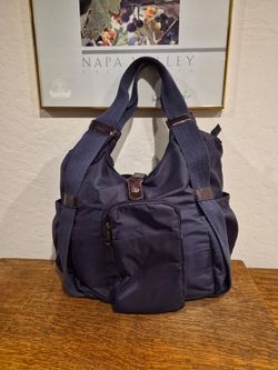 Tote bag features wide canvas straps and a front zipper pocket.
