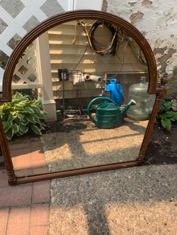 Vintage arched mirror has a brown wood frame with a fluted design. The top is a rounded arch with a visible seam at the peak. Decorative turned finia