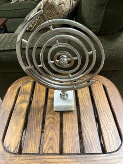 Silver-tone metal armillary sphere or astrolabe sculpture featuring concentric orbital rings and a central sphere mounted on a white marble base