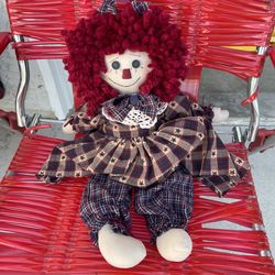 collectible rag doll with distinct red yarn hair and a plaid outfit. Features handmade styling with fabric and yarn construction. The outfit includes