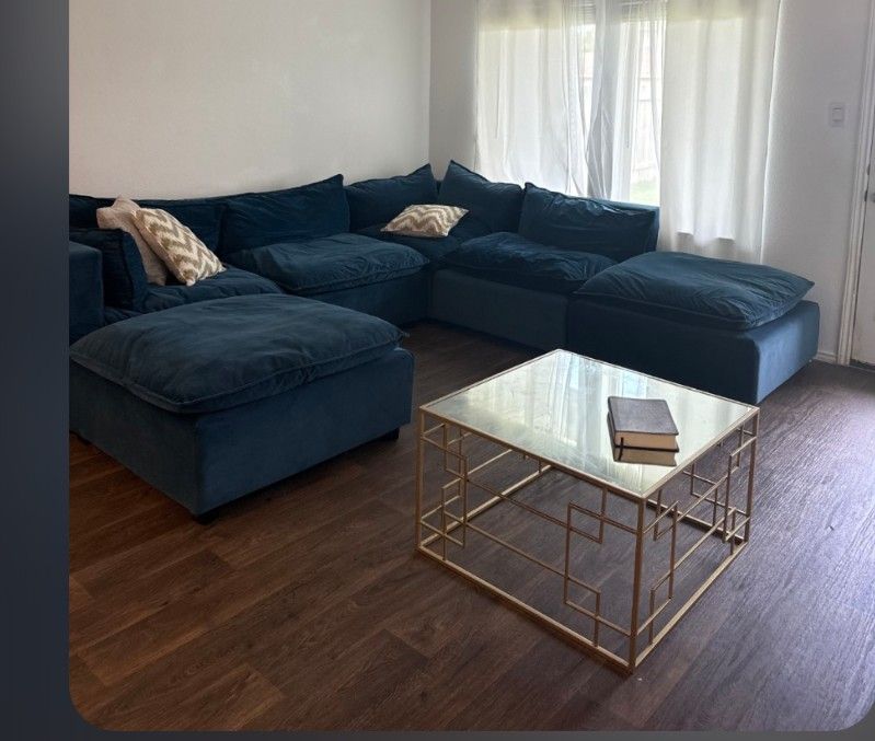 This living room features a modular, oversized blue sectional and a geometric gold coffee table with a glass top.
Sectional Sofa
The sofa is a modular
