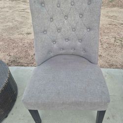 gray fabric upholstered dining side chair with a button-tufted backrest and dark wood legs. 