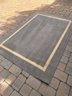 5 x 7’ Solid plush area rug with a contrasting cream inset border. It features a soft, dense tufted texture in a neutral slate or medium gray color to