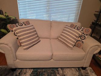Beige Fabric Loveseat with Accent Pillows and side table.