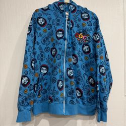 Disney Coco zip-up hoodie. Bright blue base with repeating skull and floral artwork. Embroidered Coco logo on chest. Hood and front pockets. Casual, t