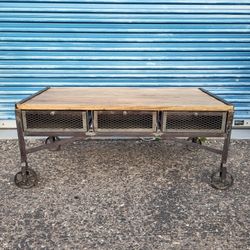 Rustic industrial style coffee table on wheels. Metal body with wood top. 3 metal basket syle drawers 