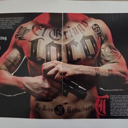 The image is a magazine spread featuring a man with tattoos on his torso and arms, holding a handgun