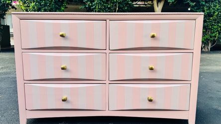 Six-drawer dresser with pink stripes and gold knobs.
