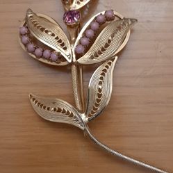 flower brooch  done in a gold finish in a cannetille filigree design and  set with mauve beads & a mauve rhinestone