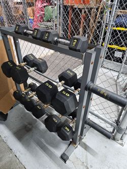 Black rubber hex dumbbell set with pairs in 10, 15, 20, 30, 40, and 50 lbs, stored on a gray steel 3-tier dumbbell rack. The rack shows surface rust a