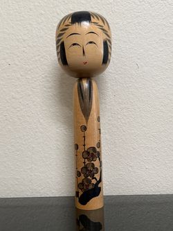 A Japanese Kokeshi doll, featuring a plum blossom motif on a slim, cylindrical wooden body, signed