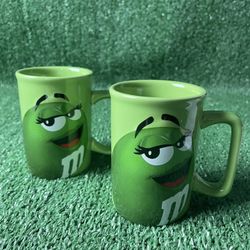 The Green M&M Ceramic Coffee Mug Cup from Mars is a collectible advertising item created in 2012. This original set of two mugs features the iconic M&