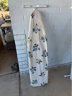 ironing board cover featuring a cream-colored fabric with blue, purple, and yellow floral patterns and subtle white polka dots.