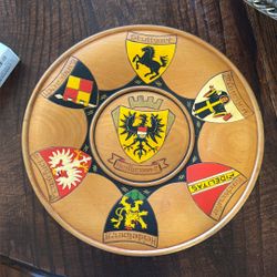 This item is a decorative wooden plate featuring various German coats of arms, likely a souvenir item from the region.  Design: The plate showcases se