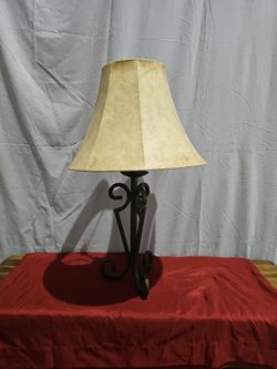 This is a rustic wrought iron table lamp featuring an artistic scrollwork tripod base and a warm, parchment-style em