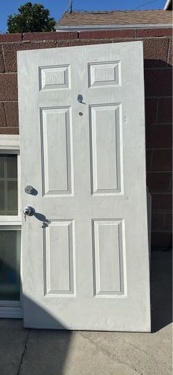 Durable white 6-panel exterior door is constructed from steel or fiberglass. It has a wood-grain texture and includes a silver-tone doorknob, deadbolt