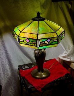 Beautiful Tiffany-style table lamp features a green leaded glass shade with purple and white geometric accents and a dark bronze base.
